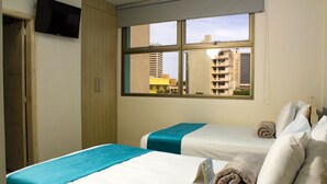 Une chambre d’hôtel avec deux lits, un téléviseur fixé au mur et une fenêtre donnant sur la ville.