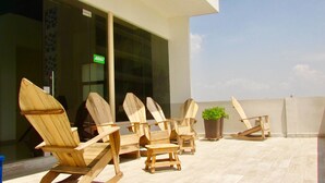 Des chaises en bois et une petite table sont disposées sur une terrasse offrant une vue sur un immeuble.