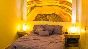 A bedroom with a bed, purple bedding, two bedside lamps, and a large abstract painting on the wall. - Ka Suites Tulum by HA (Tulum)