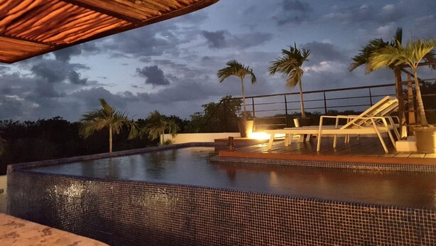 A swimming pool with a tiled edge, palm trees, and a thatched roof structure. - Ka Suites Tulum by HA (Tulum)