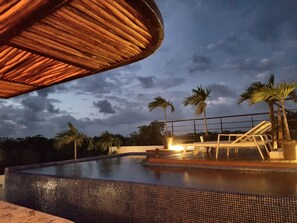 A swimming pool with a tiled edge, palm trees, and a thatched roof structure. - Ka Suites Tulum by HA (Tulum)