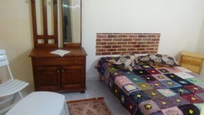 A bedroom with a bed, a wooden dresser, a white chair, and a patterned rug. - Studio Pour Vacance A Hammam Al Ghezéze (Hammam Al Agzaz)