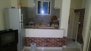 A compact kitchen with a refrigerator, a small window, and a brick backsplash. - Studio Pour Vacance A Hammam Al Ghezéze (Hammam Al Agzaz)
