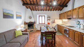 Una sala de estar acogedora con chimenea, mesa de comedor y zona de cocina con alacenas de madera y salpicadero de azulejos.