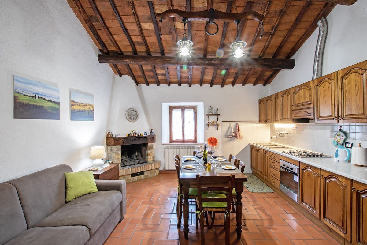 A cozy living room with a fireplace, a dining area with a table set for four, and a kitchen with wooden cabinets and a gas stove.