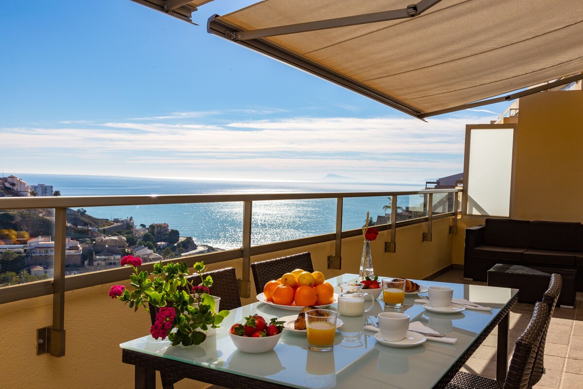 A balcony with a table set for breakfast, overlooking a coastal view.