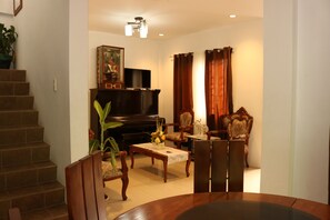 A living room with a piano, television, and dining area with chairs and a table. - Casa Purisima (Tagaytay)