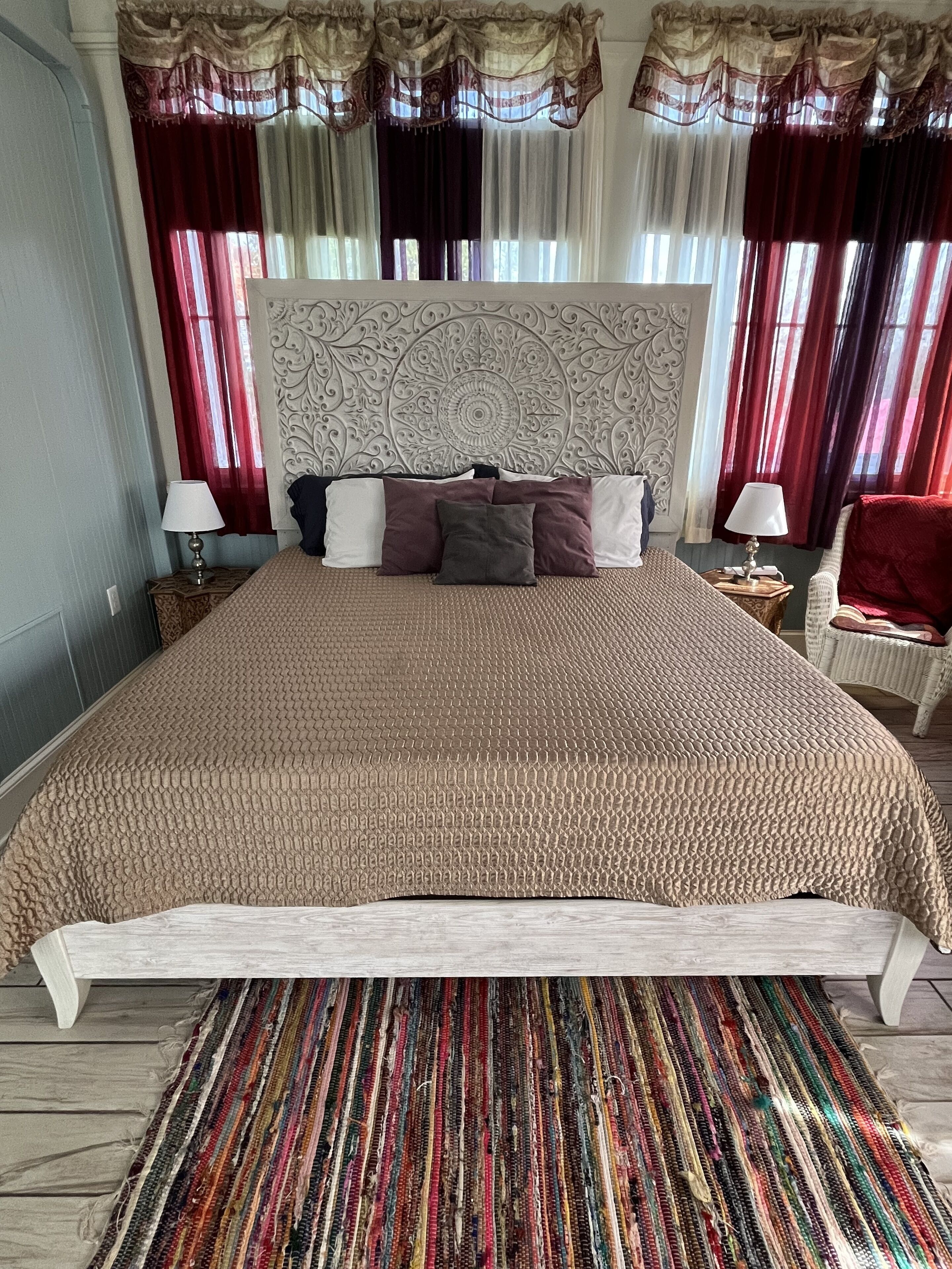 A large bed with a textured beige bedspread, a decorative headboard, and a colorful striped rug.