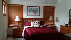 A bedroom with a wooden bed, two bedside tables with lamps, a framed picture on the wall, and a dresser. - Beautiful home, hot tub, across from Camelback Resort (Tannersville)