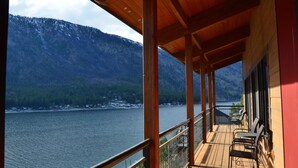Terraza de madera con asientos al aire libre, con vista a un lago y montañas.