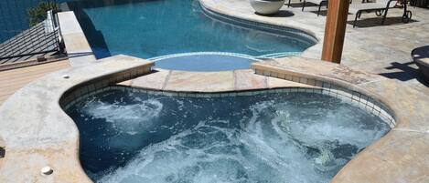 A swimming pool with a hot tub, lounge chairs, and potted plants.