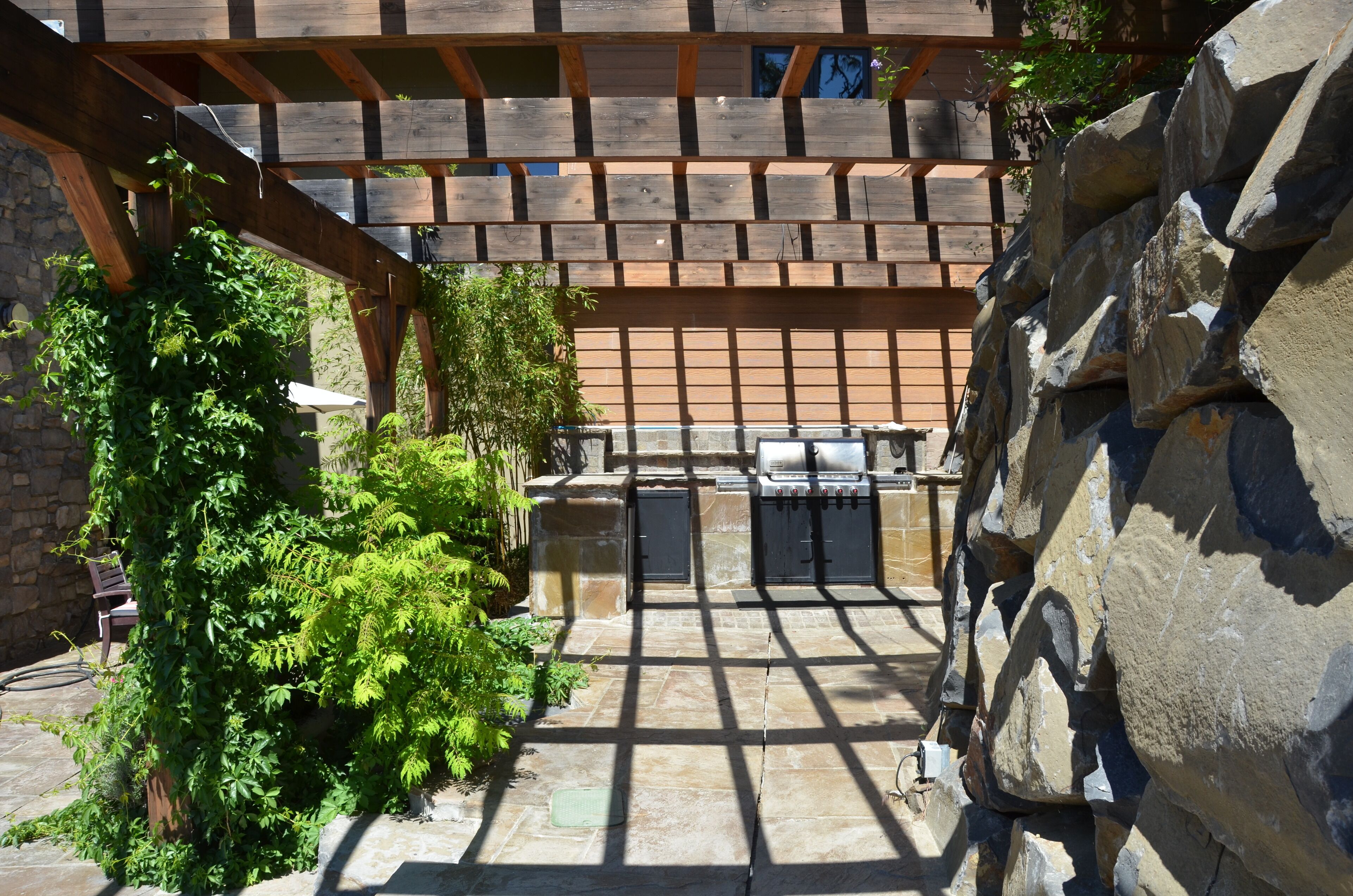 Une terrasse extérieure dotée d’un sol en pierre, d’une pergola en bois et d’un mur en pierre.