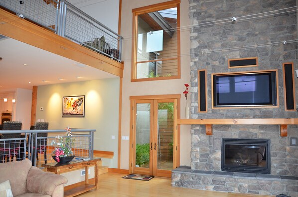 A spacious living area with a stone fireplace, a television mounted above it, and a balcony with a railing.