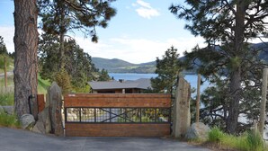 Propiedad amurallada con cerca de madera, portón metálico y vista a un lago y montañas.