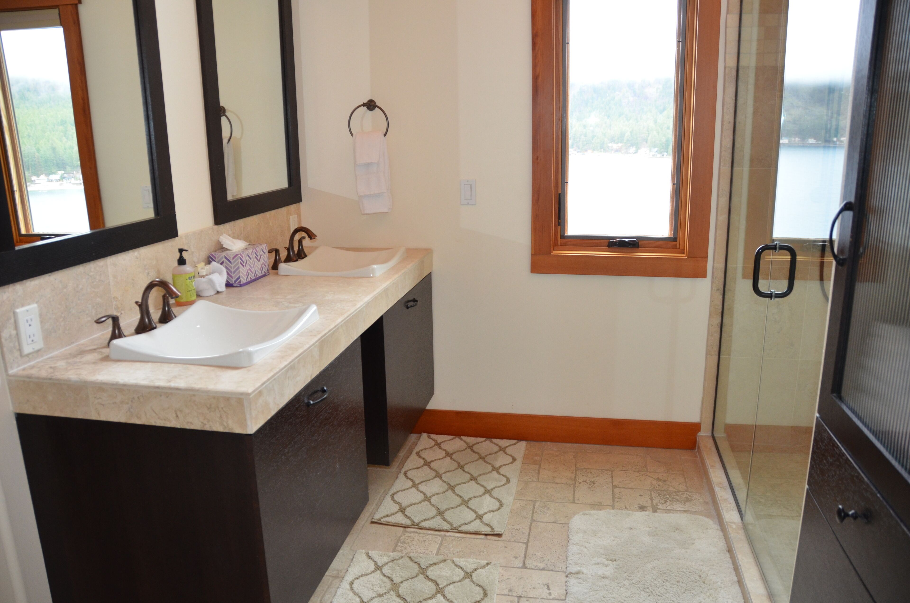 A bathroom with two sinks, a mirror, a towel rack, and a window with a view of a body of water.