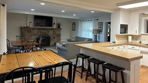 A modern kitchen with a stone fireplace, wooden dining table, and bar stools. - Huge Private Sandy Beach! Sleeps 22! Private Suites! Some Aug/Sept Availability! (Onaway)