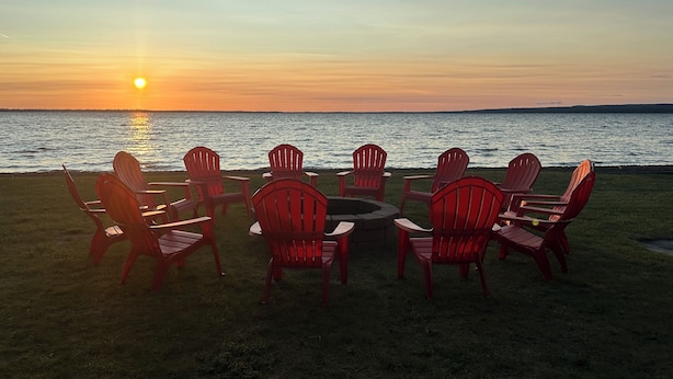 A sunset view with a fire pit and red chairs facing the water. - Huge Private Sandy Beach! Sleeps 22! Private Suites! Some Aug/Sept Availability! (Onaway)