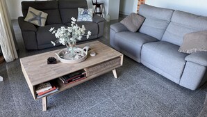 Ett vardagsrum med en grå soffa, ett soffbord med en vas med blommor och en bokhylla.
