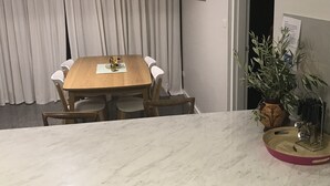 En matplats med ett träbord och stolar, en bänkskiva i marmor, en krukväxt och en dörr med en skylt.