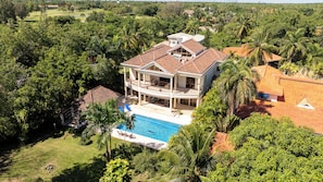 Una casa grande con piscina, rodeada de abundante vegetación.