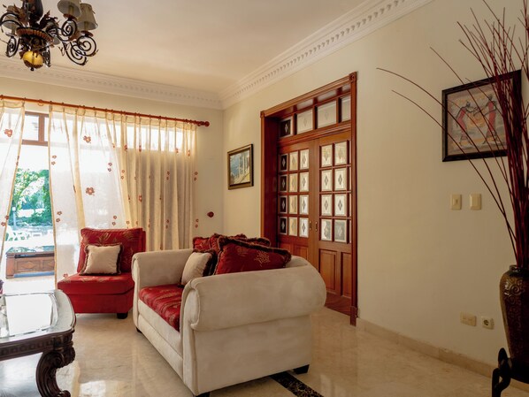 A room with a sofa, a table, a chandelier, a door with glass panels, and a painting on the wall. - Golf Mora Luxury Villa (Metro Country Club Juan Dolio)