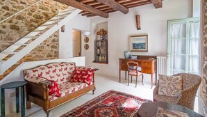 A cozy living room with a wooden sofa, a patterned rug, a desk, and a bookshelf. A staircase with exposed wooden beams leads to another level. - Charm, comfort, relax at il Bracconiere, part of il Cavato, typical farmhouse
, (Poggio Alla Croce)