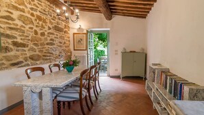 A dining area with a stone wall, wooden chairs, a marble table, and a bookshelf with books. - Charm, comfort, relax at il Bracconiere, part of il Cavato, typical farmhouse
, (Poggio Alla Croce)