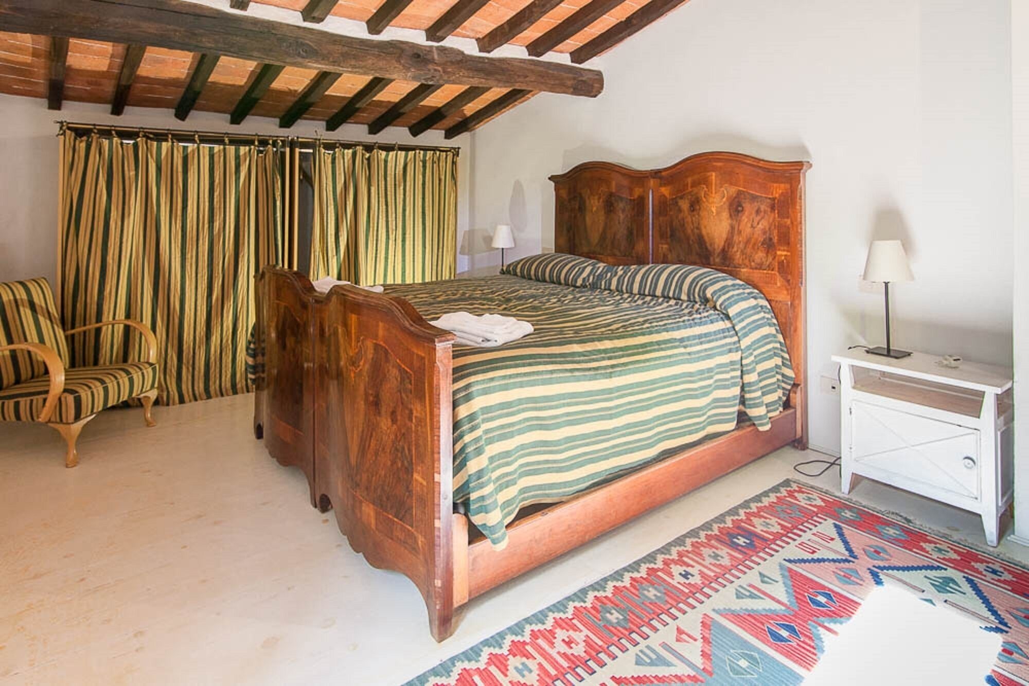 Une pièce avec un lit en bois, une chaise, une table de chevet et un tapis à motifs.