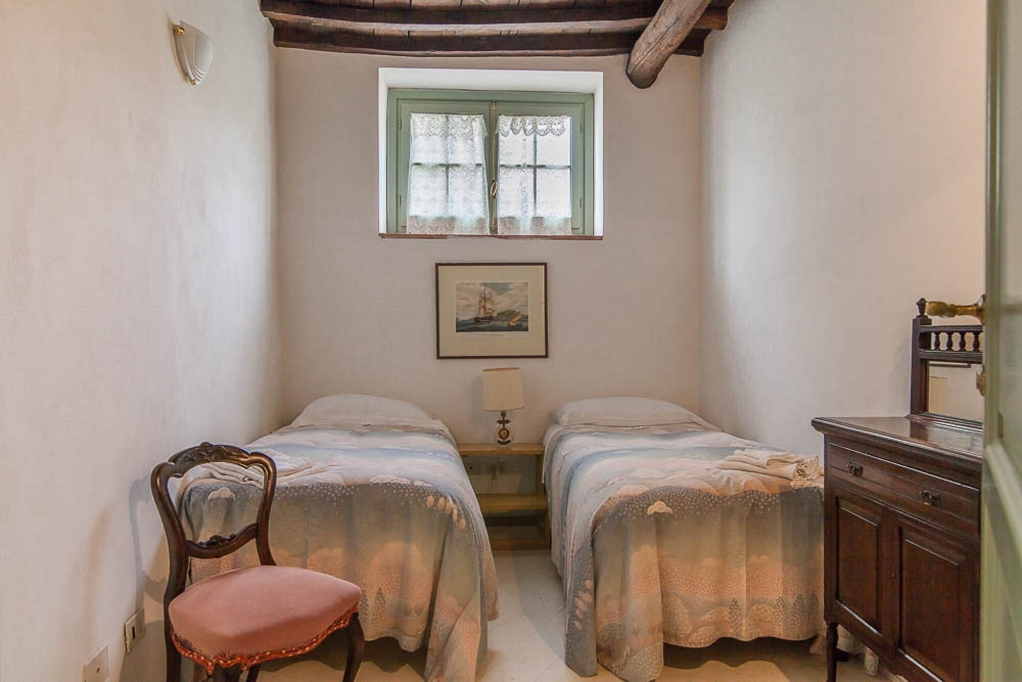 Un dormitorio pequeño y acogedor con dos camas individuales, una silla, una mesita de noche y un aparador.