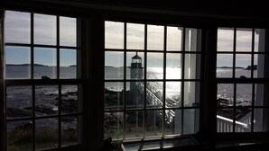A view through a window with a grid pattern, overlooking a rocky shoreline with a lighthouse and distant landforms. - "Tranquility Base" is a place where you can lose yourself in nature. (St George)