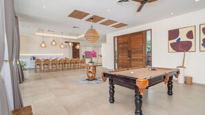 A spacious living area with a pool table, a dining area with chairs, and a kitchen in the background.