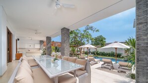 A modern outdoor living area with a glass-top table, wicker furniture, and a poolside setting.