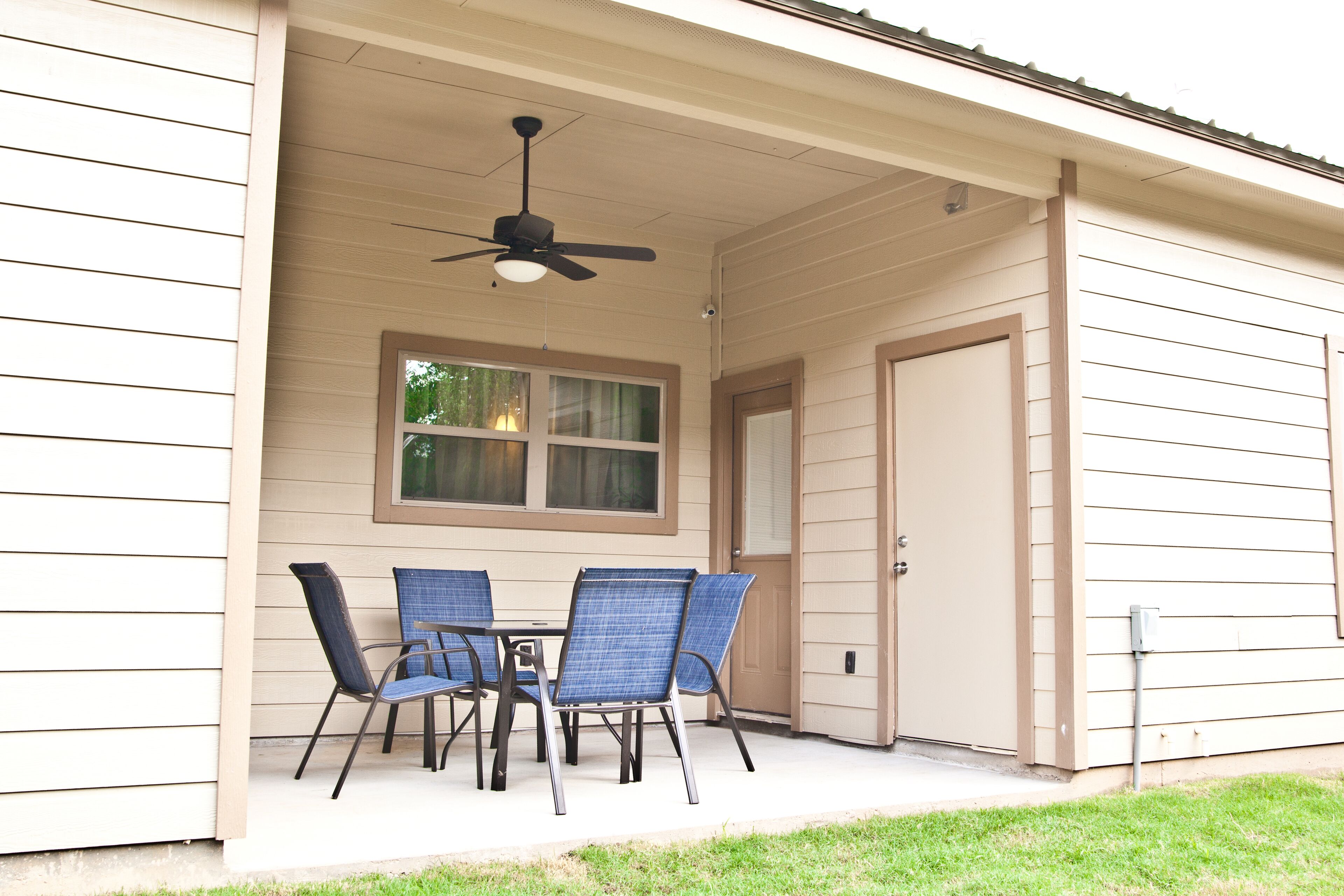 A covered patio with a table and chairs, a ceiling fan, and a window.