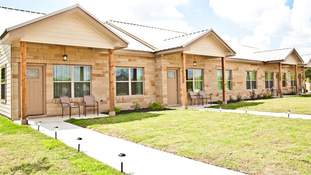 A row of single-story buildings with a brick facade, large windows, and outdoor seating areas. - "The Indigo" A little bit country, close to town.  New, clean and fresh looking (Kyle)