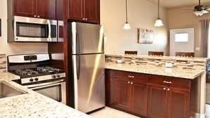 A kitchen with stainless steel appliances, wooden cabinets, granite countertops, pendant lighting, and a tiled backsplash. - "The Indigo" A little bit country, close to town.  New, clean and fresh looking (Kyle)