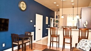 A living room with a dark blue wall, wooden furniture, and a kitchen in the background. - "The Indigo" A little bit country, close to town.  New, clean and fresh looking (Kyle)