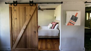 Un dormitorio con puerta corredera de madera, una cama con almohadas y una obra de arte colgada en la pared.