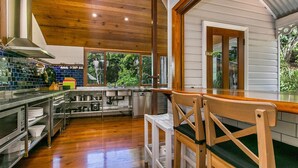 Une cuisine moderne avec un plancher en bois, des appareils électroménagers en acier inoxydable et une grande fenêtre donnant sur un paysage verdoyant.