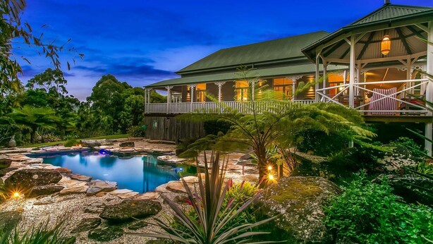 Une grande maison avec une piscine, entourée de rochers et de plantes.