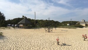 Ein sandiger Strand mit einem Kiosk, Spielgeräten und einem Haus im Hintergrund.