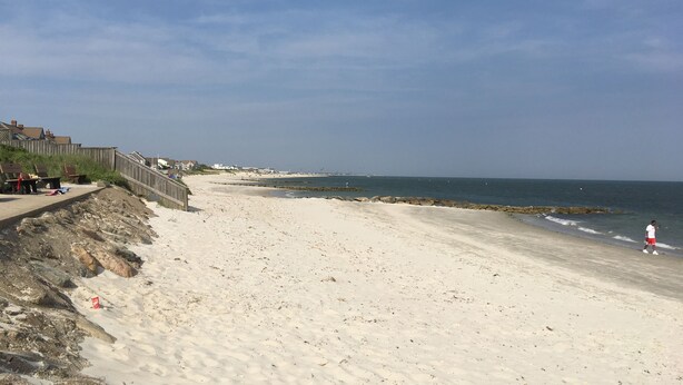 Ein Strand mit einem Holzsteg, felsigem Ufer und blauem Himmel.