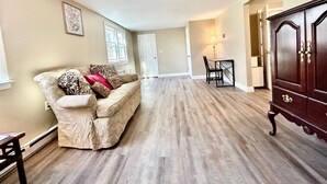 Ein geräumiges Wohnzimmer mit einem beigen Sofa, Holzboden, einer dunklen Holzkommode und einem Essbereich mit Tisch und Stühlen.