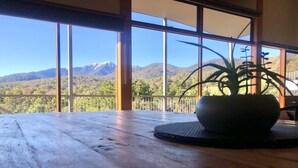 A wooden table with a potted plant in a white pot, large windows with a mountain view, and a wooden railing. - Large 6 Bedroom Family Home - Great for large groups (Merrijig)