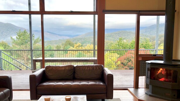 A cozy living room with a leather sofa, a coffee table with pastries, and a wood-burning stove. - Large 6 Bedroom Family Home - Great for large groups (Merrijig)