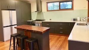 A modern kitchen with a central island, bar stools, a built-in oven, and a window above the sink. - Large 6 Bedroom Family Home - Great for large groups (Merrijig)