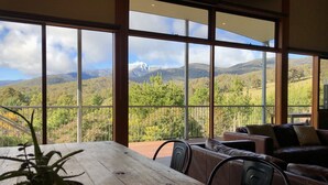 A balcony with a wooden table and chairs, overlooking a mountainous landscape with trees and a clear sky. - Large 6 Bedroom Family Home - Great for large groups (Merrijig)