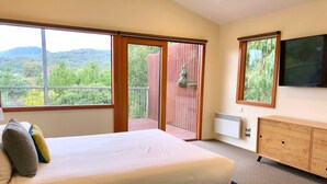A bedroom with a large bed, a wooden dresser, a television, and a balcony with a view of greenery. - Large 6 Bedroom Family Home - Great for large groups (Merrijig)