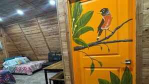 A room with a wooden ceiling, a bed with patterned bedding, a table, and a door with a bird painting.