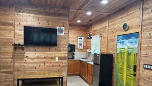 A compact kitchen with wooden walls, a built-in TV, a microwave, a refrigerator, and a sink.