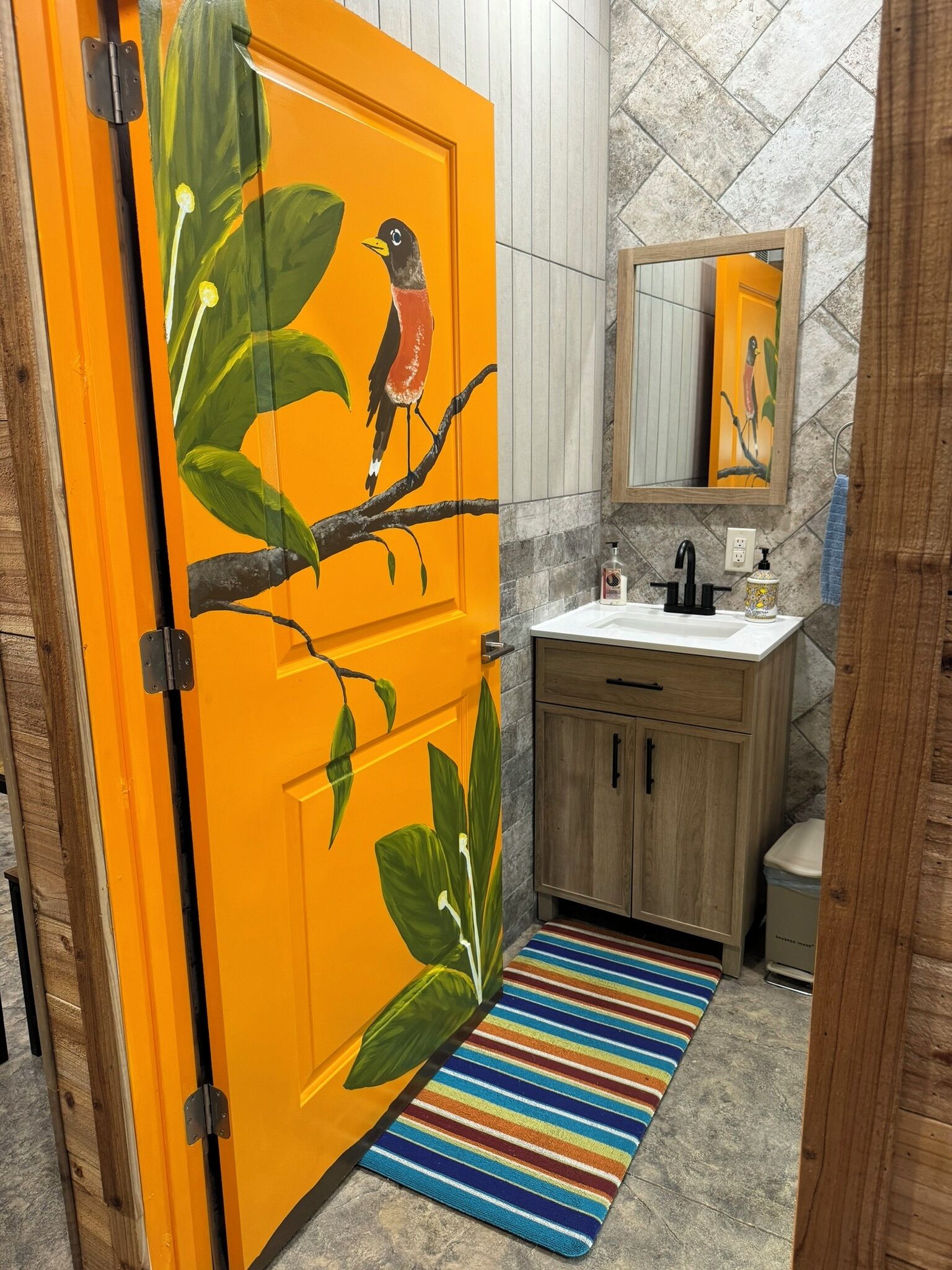 Un bagno con una porta colorata arancione, un armadietto in legno, un lavandino bianco e un tappeto a righe.